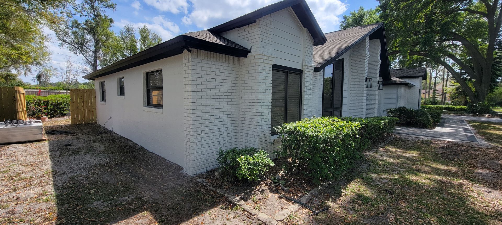 A white house with a black roof is sitting on top of a dirt field.