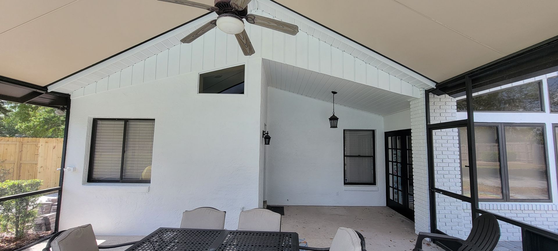 A screened in porch with a table and chairs and a ceiling fan.