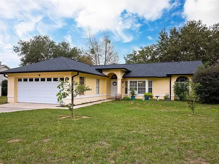 A yellow house with a black roof and a white garage door