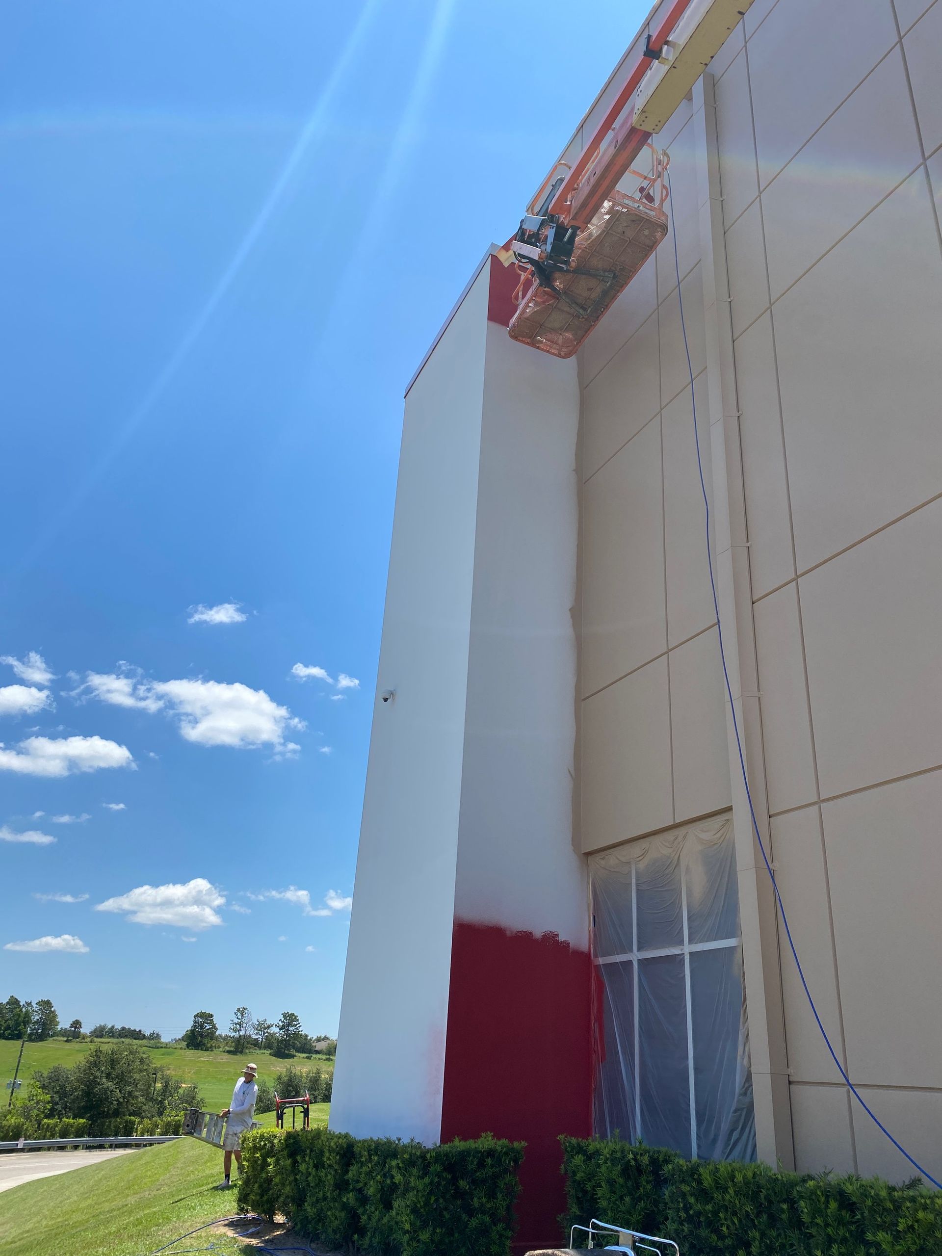 A man is painting the side of a building with a crane.