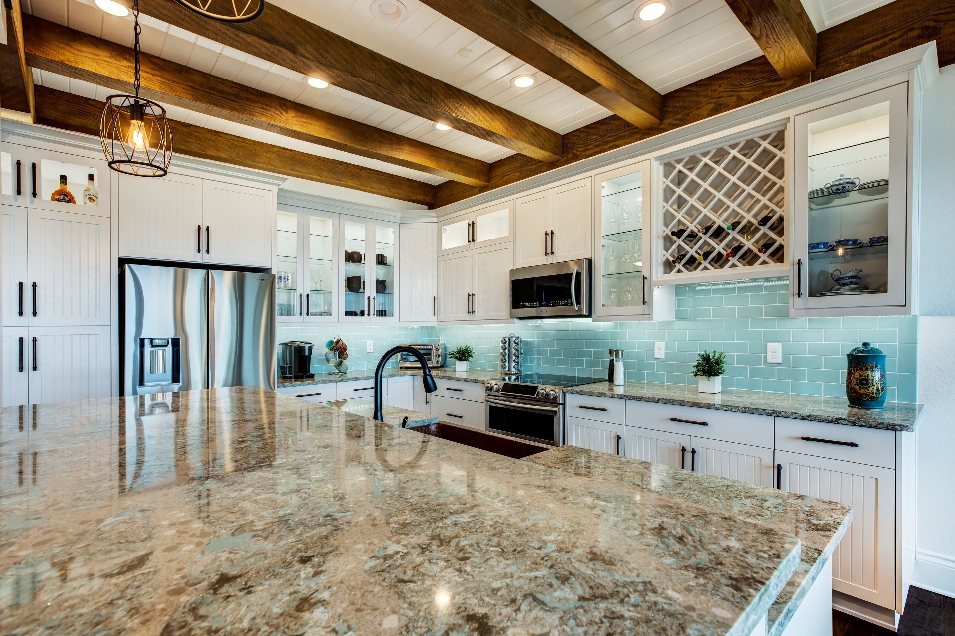 A kitchen with white cabinets , granite counter tops , stainless steel appliances , and wooden beams.