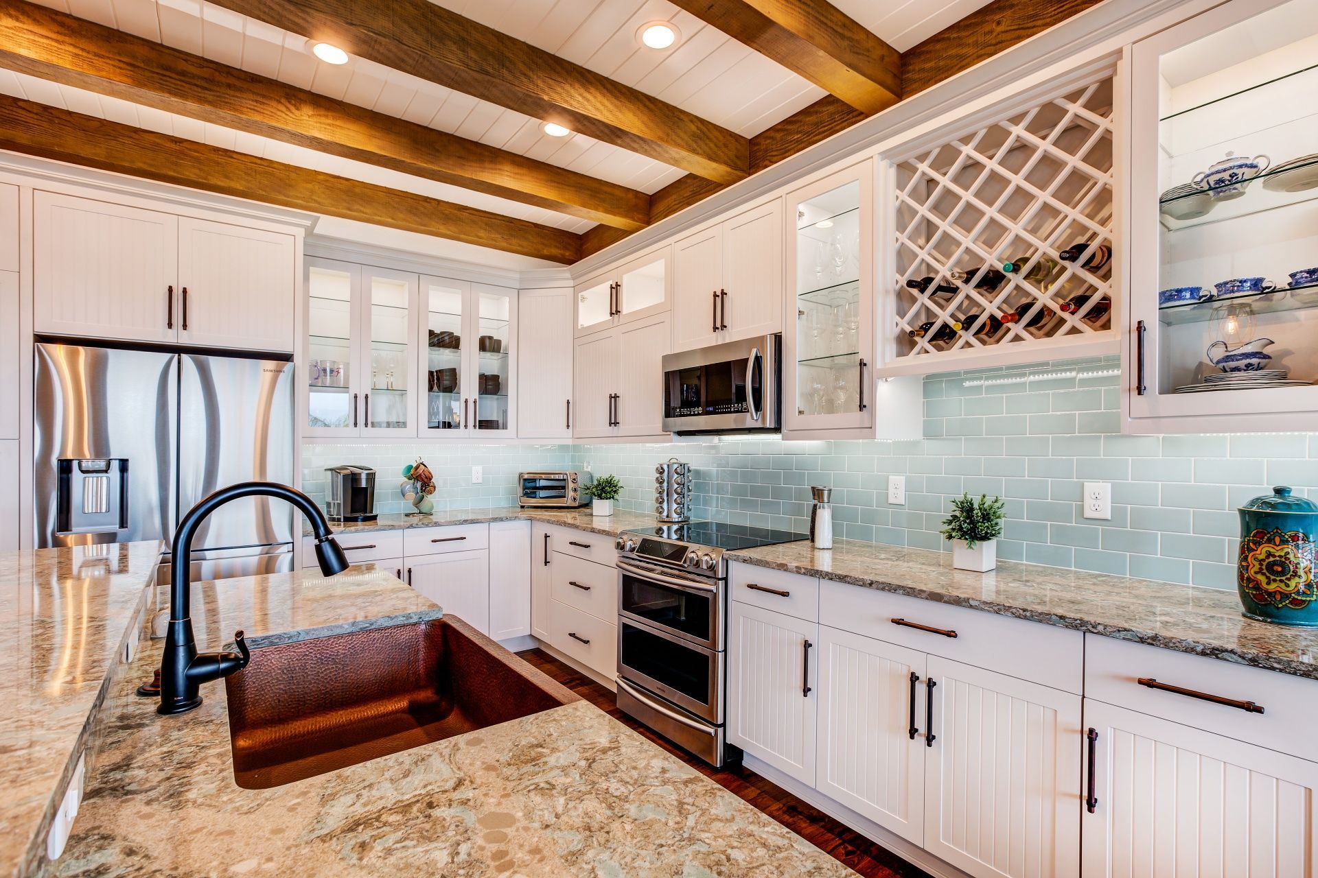 A kitchen with white cabinets , granite counter tops , stainless steel appliances and a copper sink.
