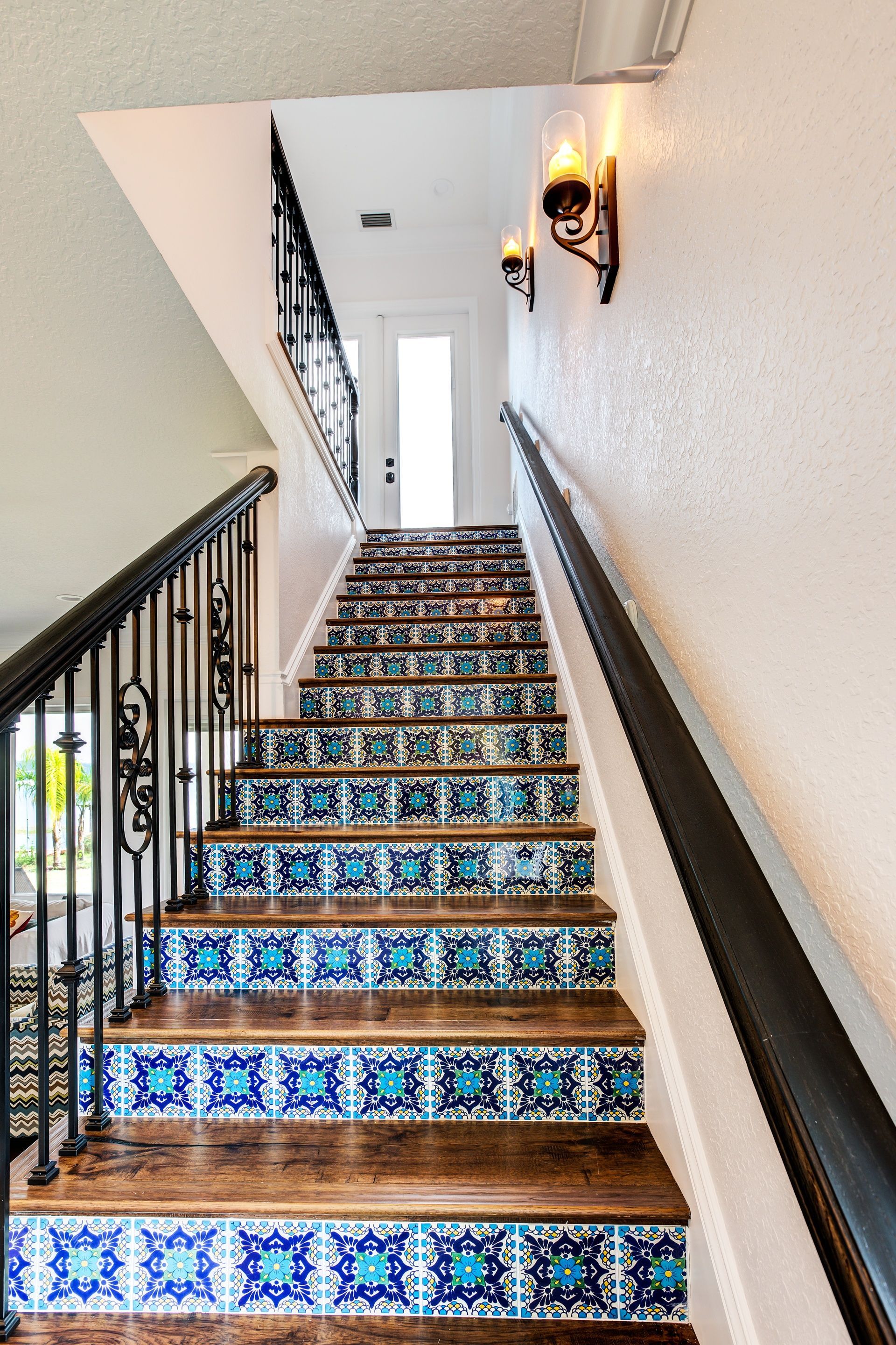 A staircase with blue tiles on the steps and a black railing.