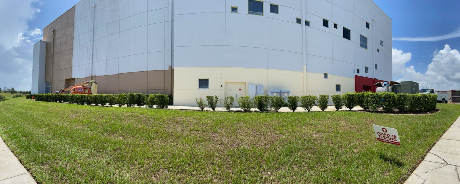 A large white building with a lot of windows is surrounded by grass and bushes.