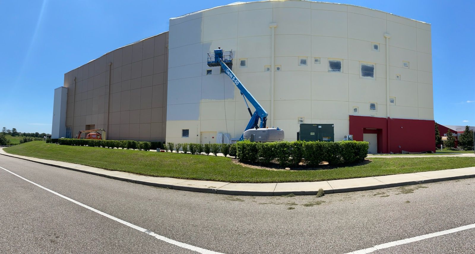 A large white building is being painted with a crane.