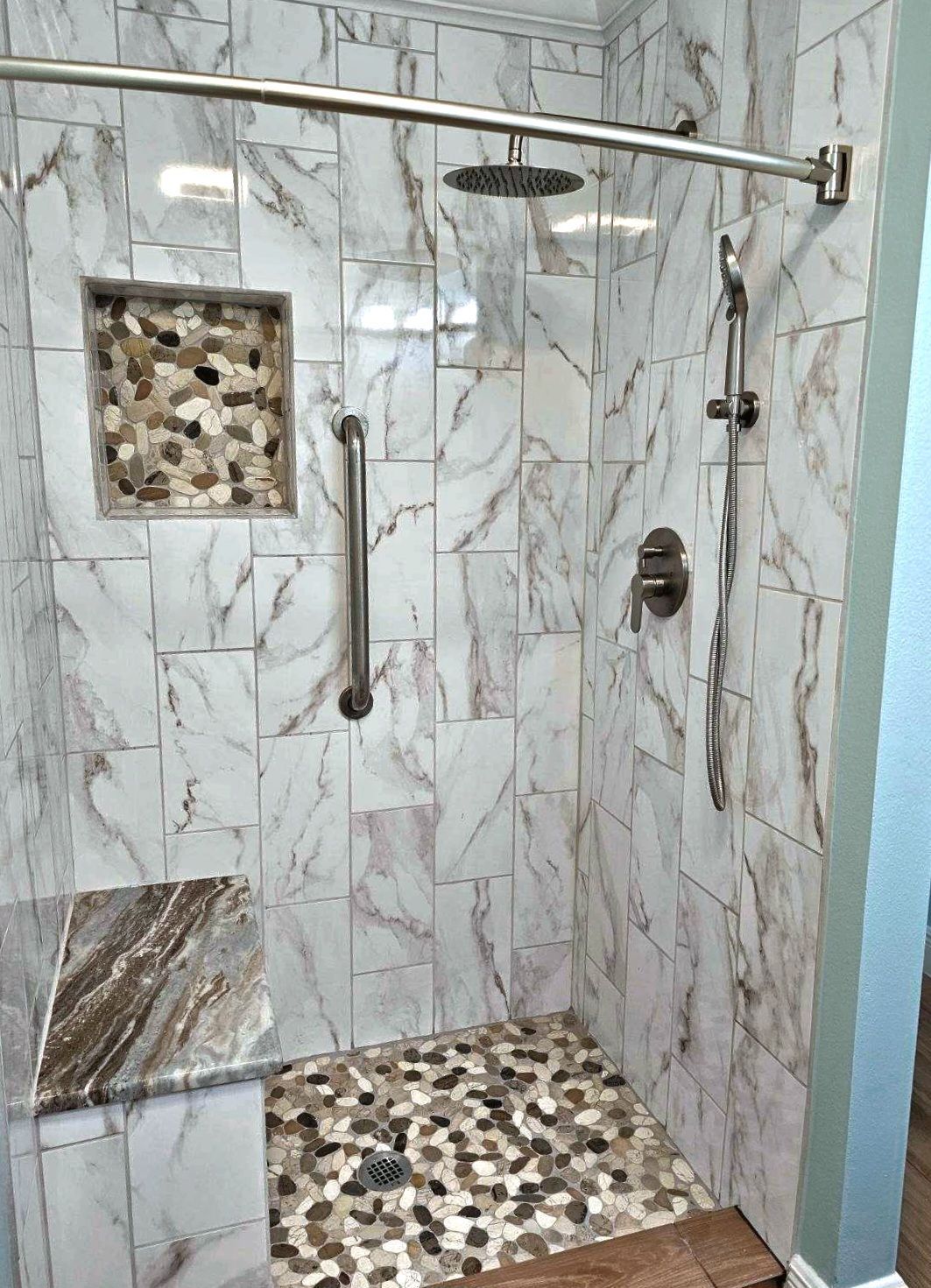 A walk in shower with marble tiles and a shower head.