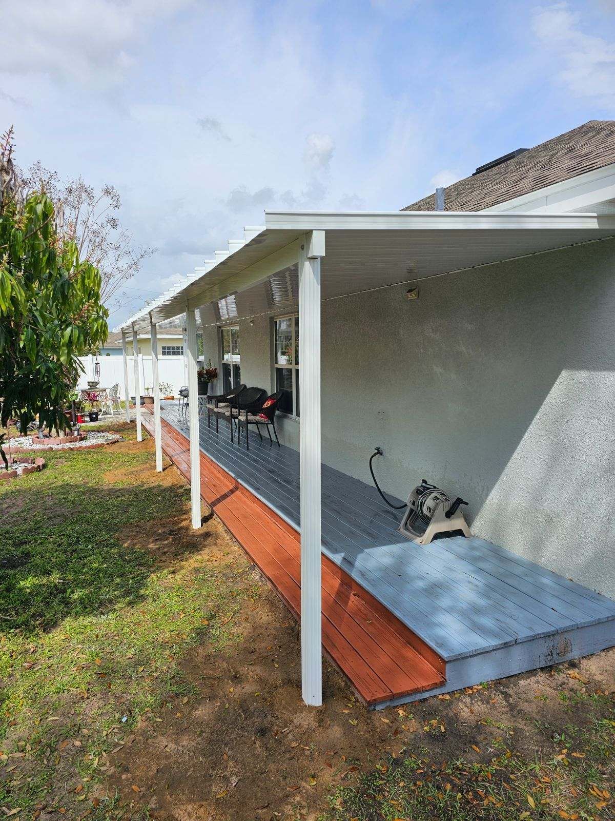 A dog is sitting on a wooden deck under a covered porch.