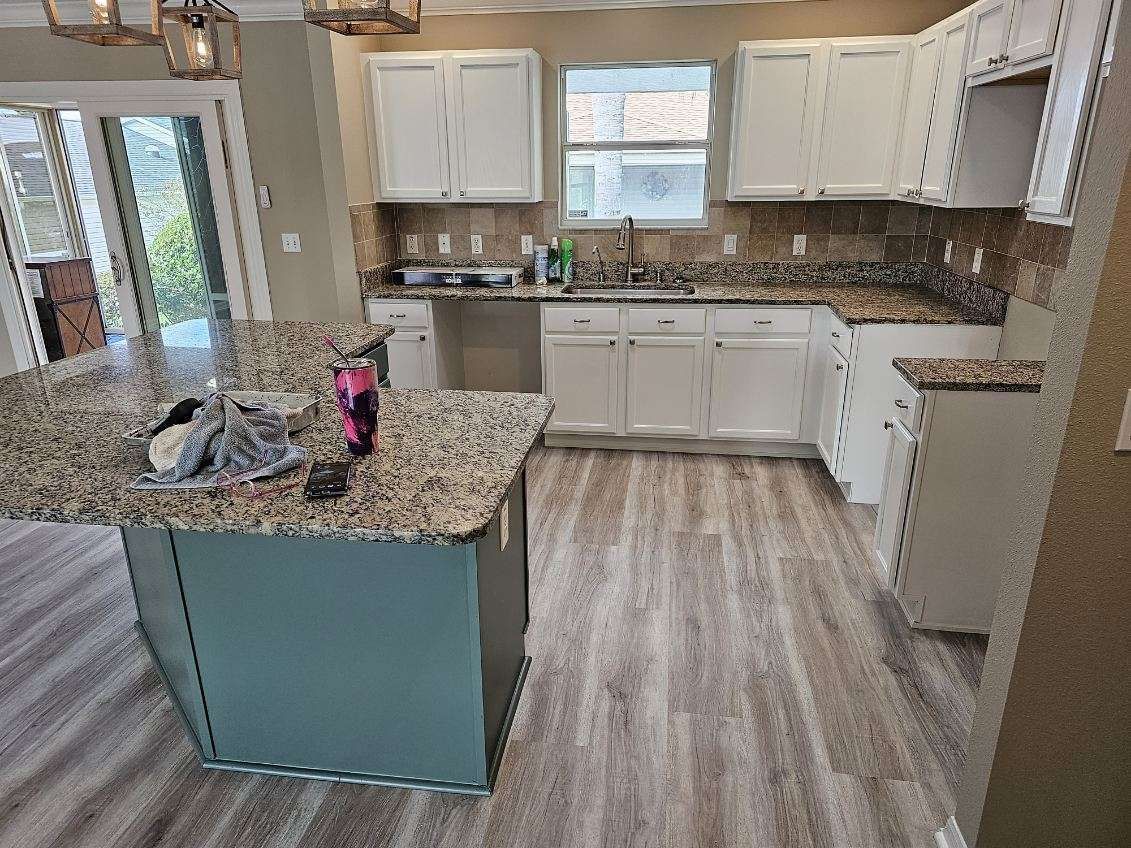A kitchen with granite counter tops , white cabinets , and a blue island.