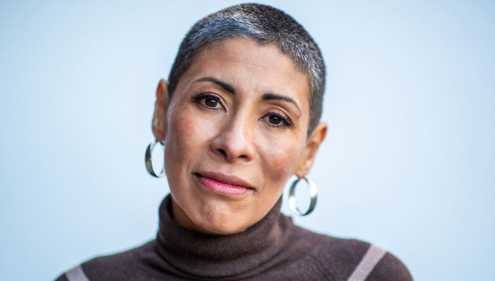 Woman with short, gray hair wearing hoop earrings and a brown turtleneck.