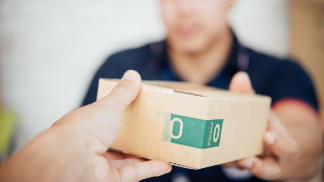 A dentist’s hand delivers a small shipping box with dental components to another person, symbolizing