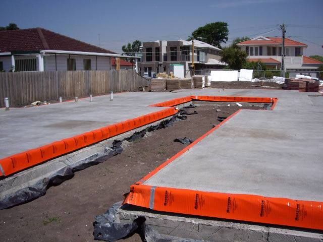 A concrete floor with orange barriers around it and a wooden fence next to it — Advanced Pest Control Wollongong in Albion Park Rail, NSW