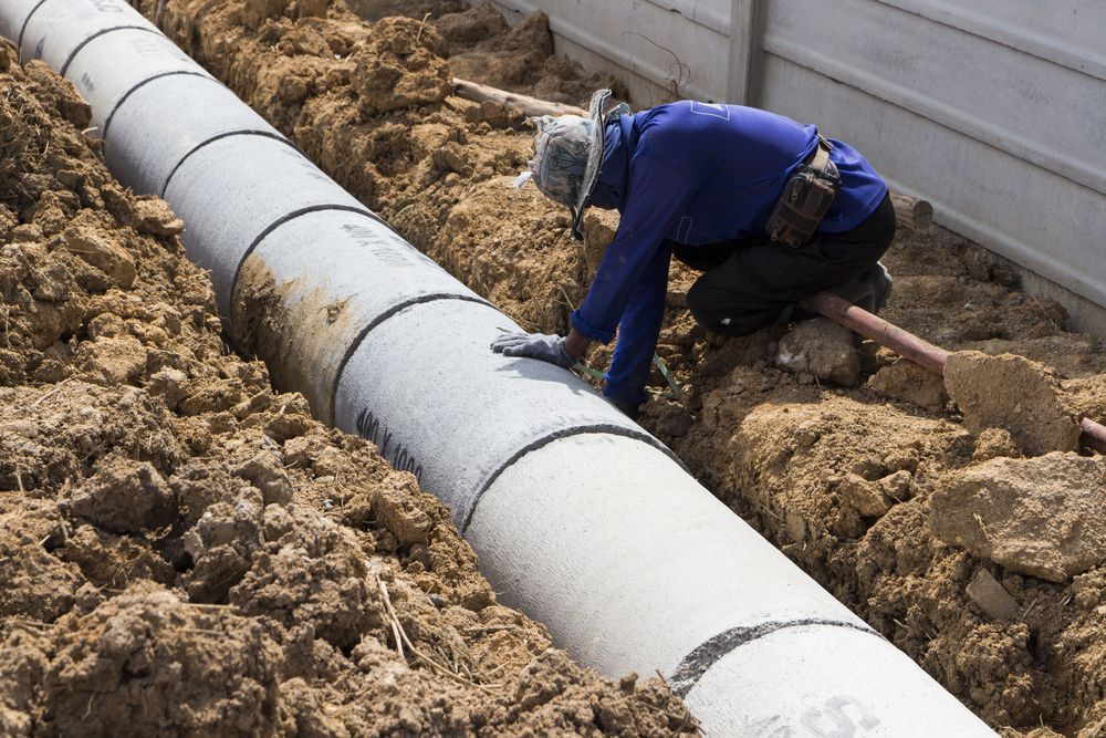 A man is kneeling down next to a pipe in the dirt — Advanced Pest Control Wollongong in Albion Park Rail, NSW