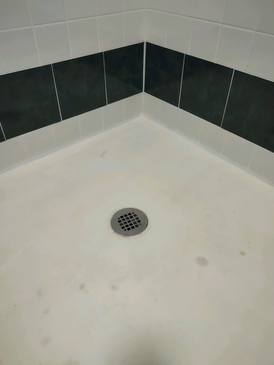A shower stall with black and white tiles and a drain