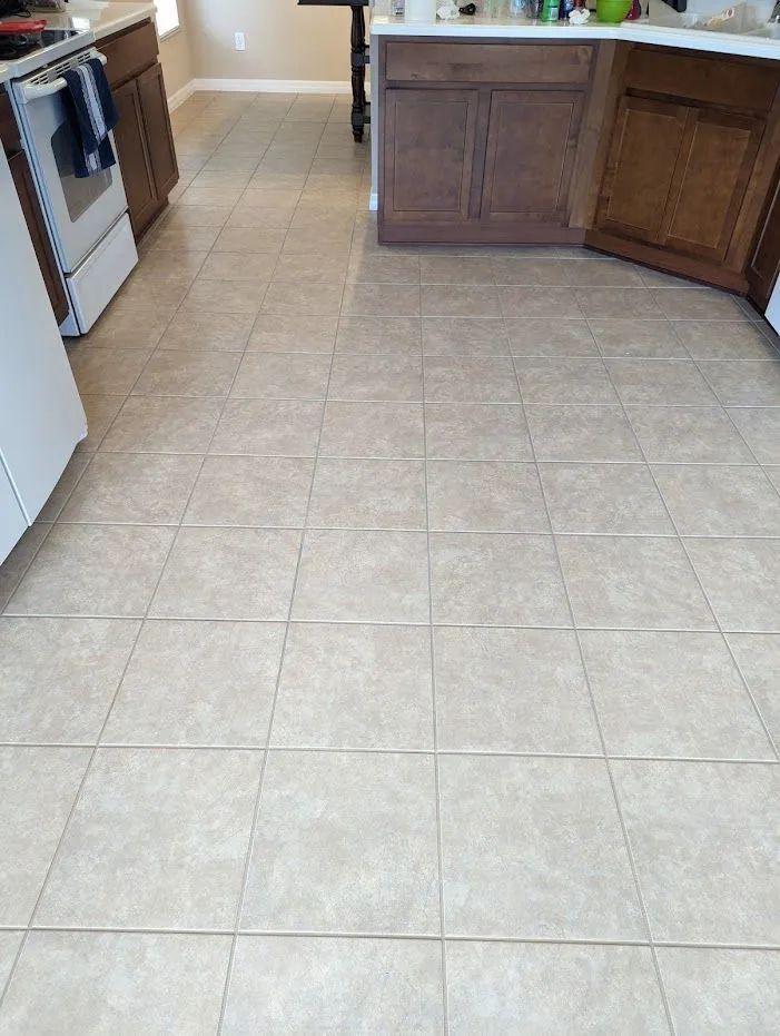 Beige tiled kitchen floor with brown cabinets and white appliances.