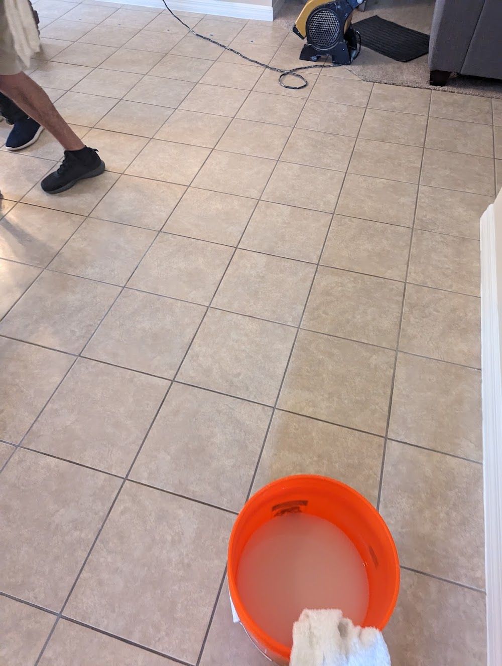 A person is standing on a tiled floor next to a bucket of water.