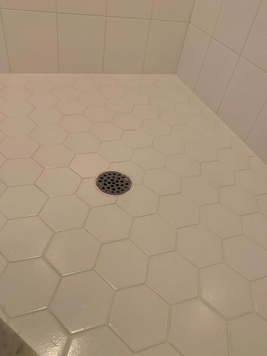 A shower stall with white tiles and a drain on the floor.