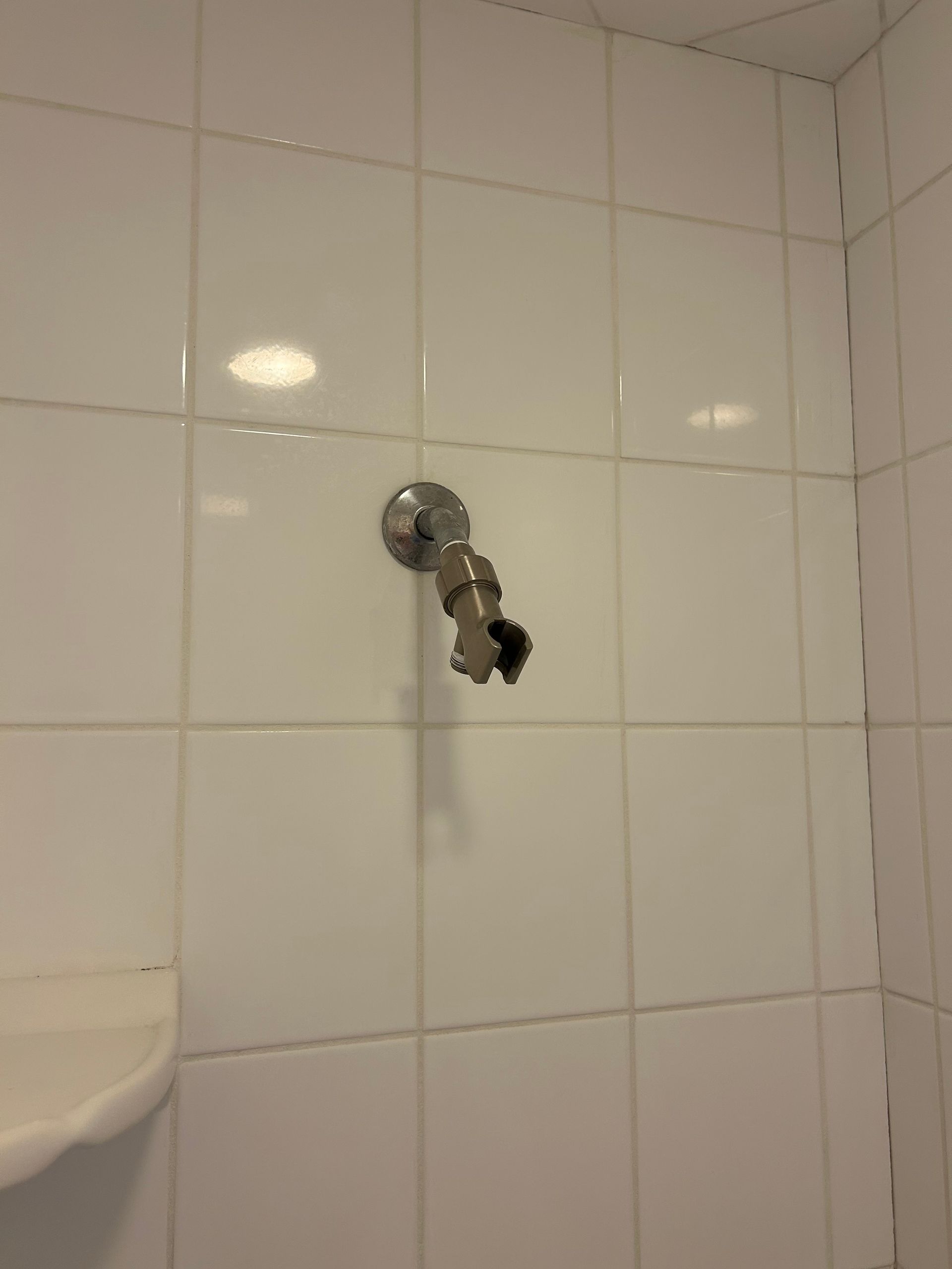 Shower faucet on white tiled wall.