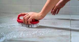 A person is cleaning a tile floor with a red brush.
