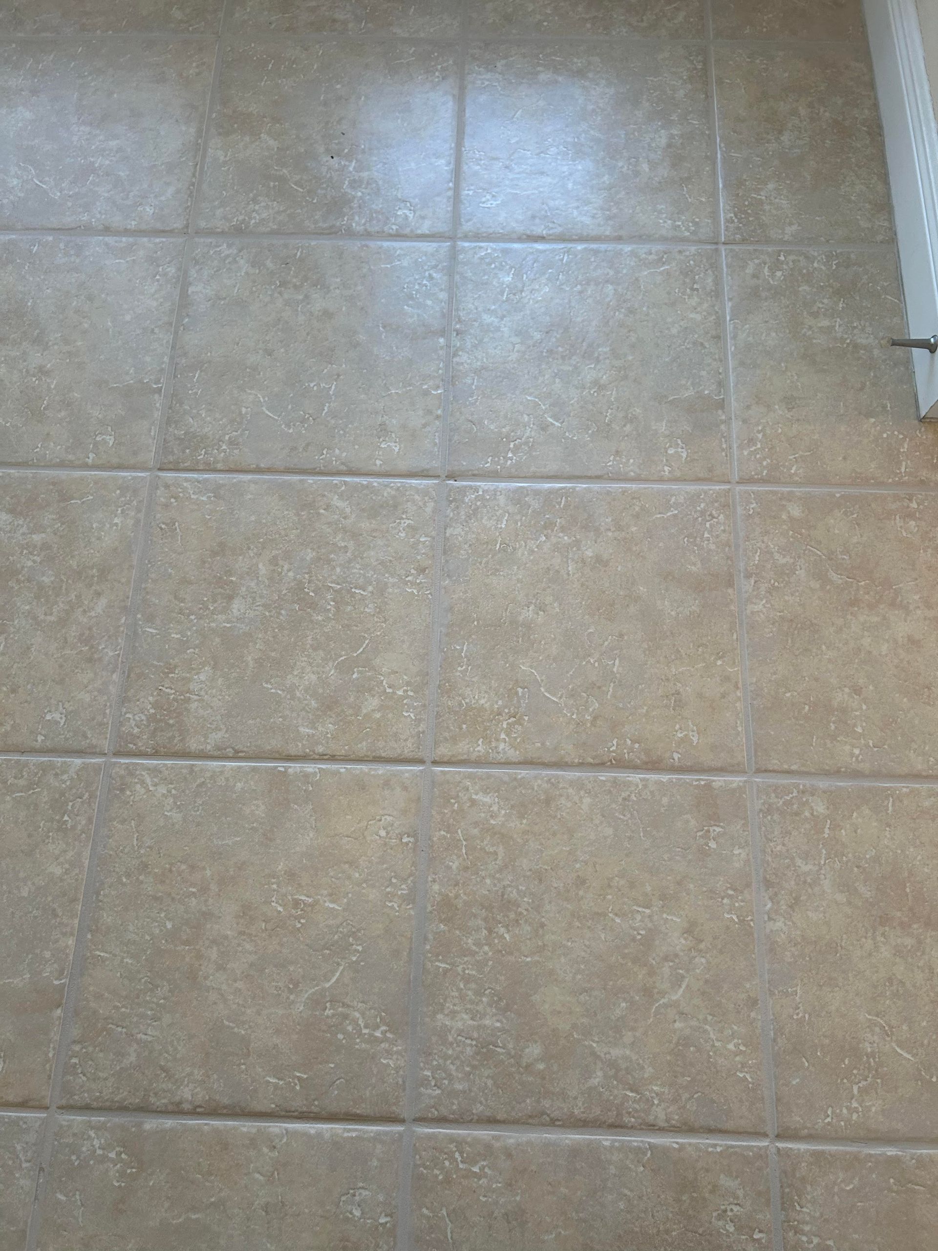 A close up of a tiled floor with a toilet in the background.