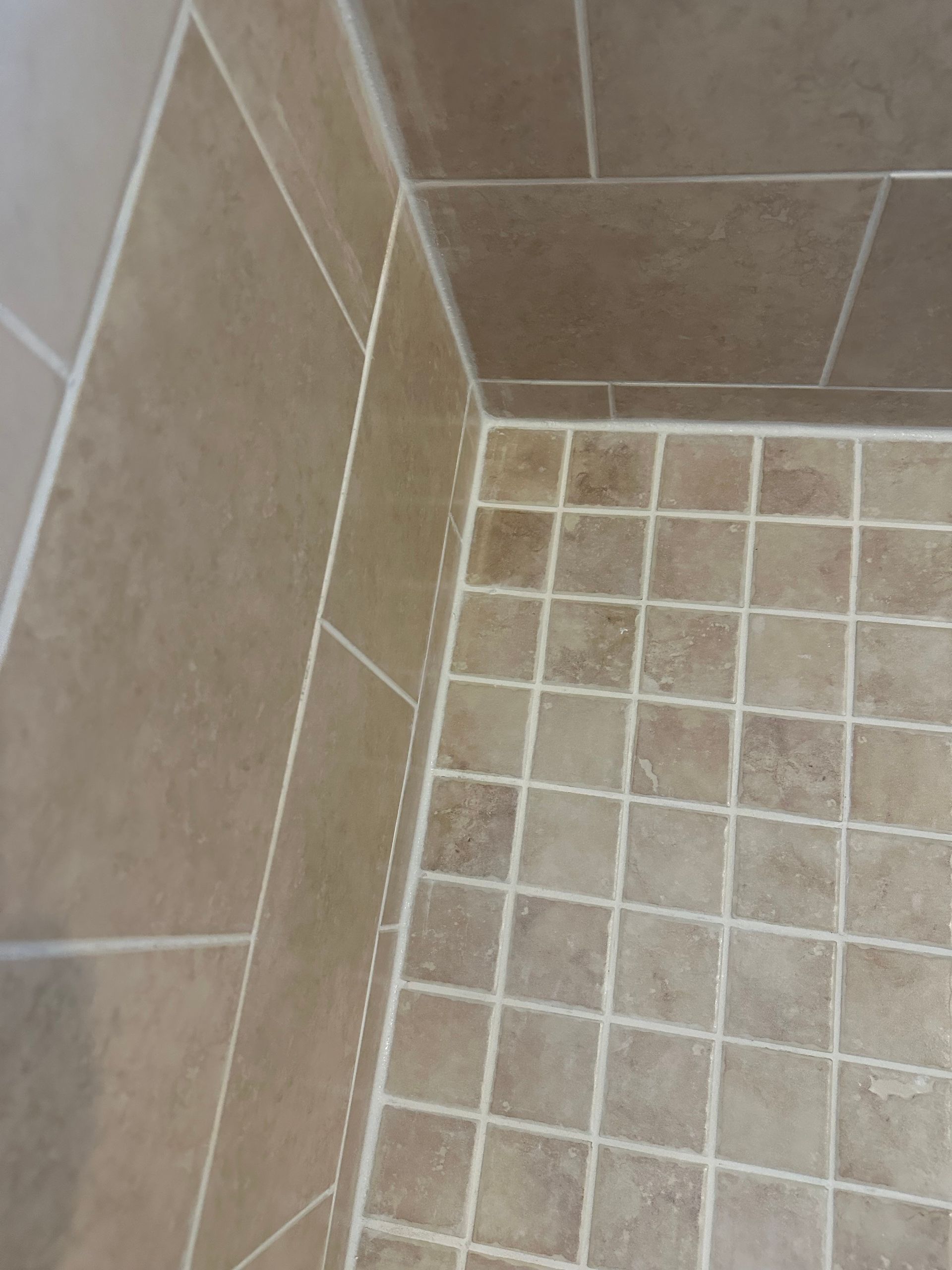 A close up of a tiled floor with a toilet in the background.