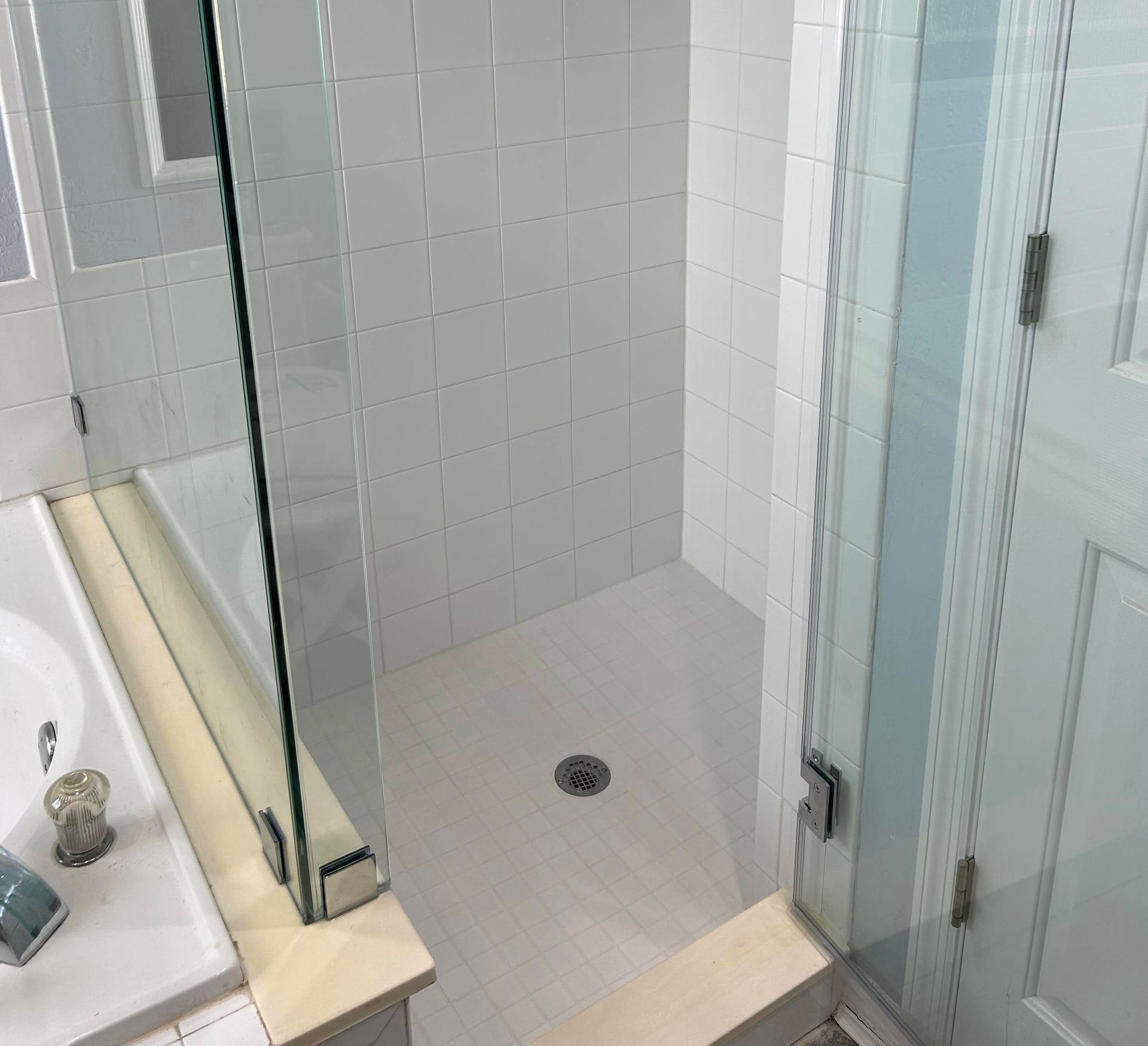 A shower stall with white tiles and a drain.