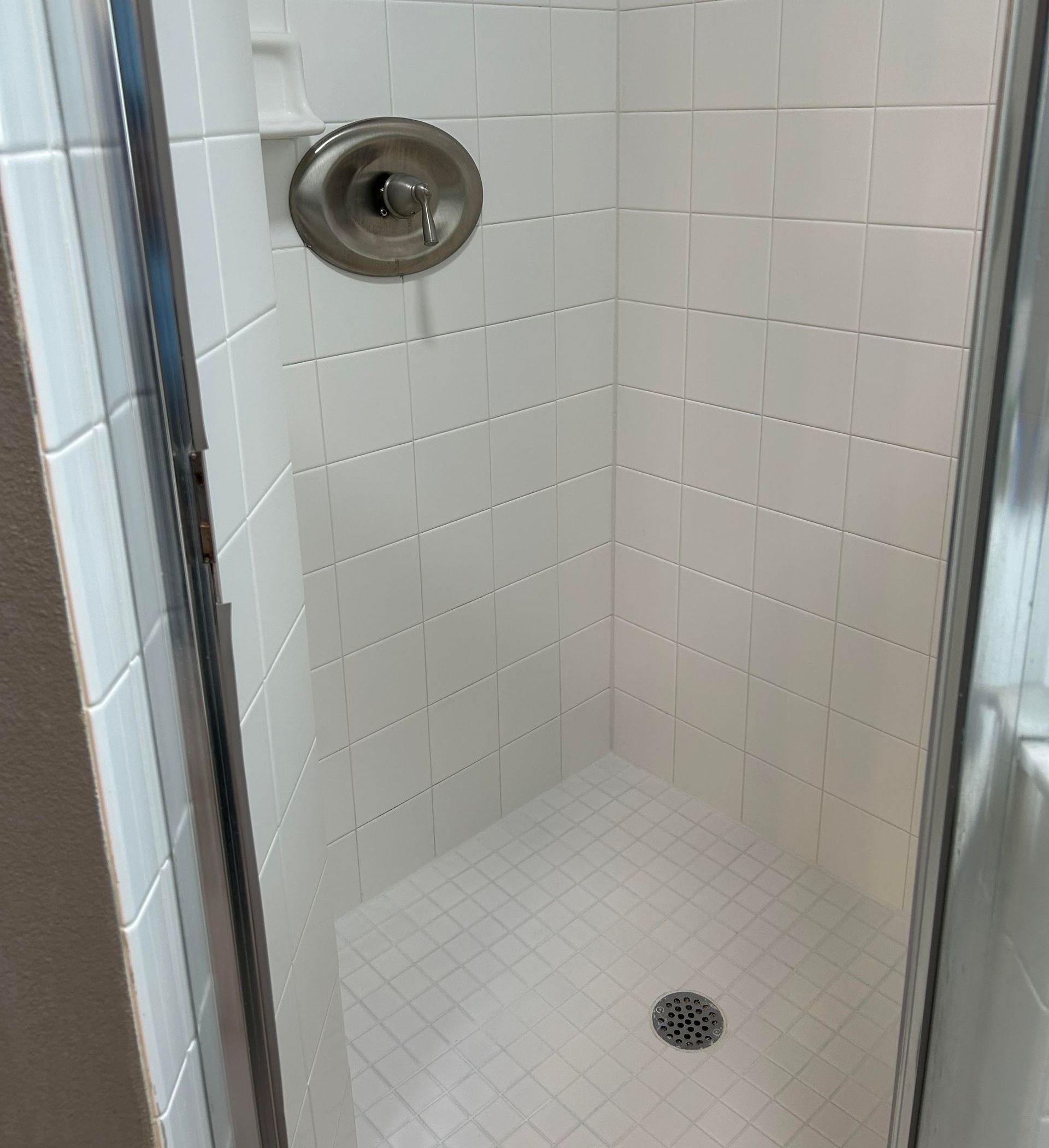 A shower stall with a glass door and white tiles in a bathroom.