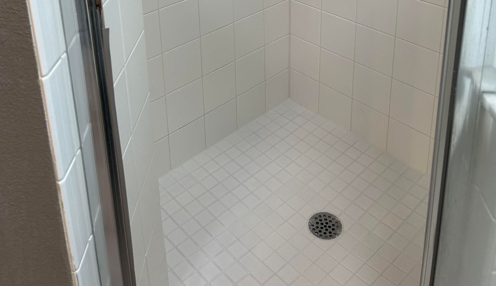 A shower stall with white tiles and a drain in a bathroom.