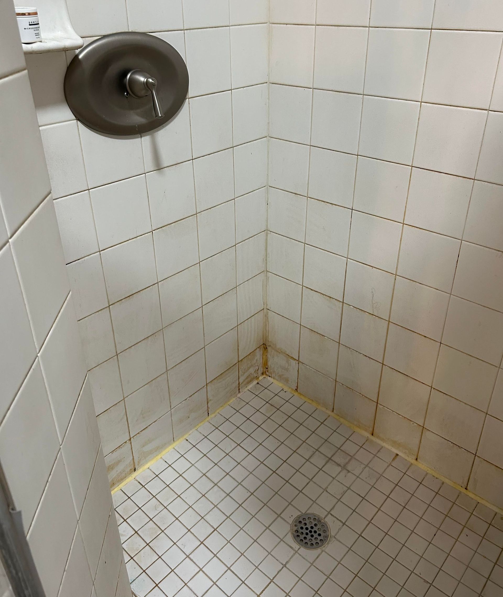 A shower stall with white tiles and a drain