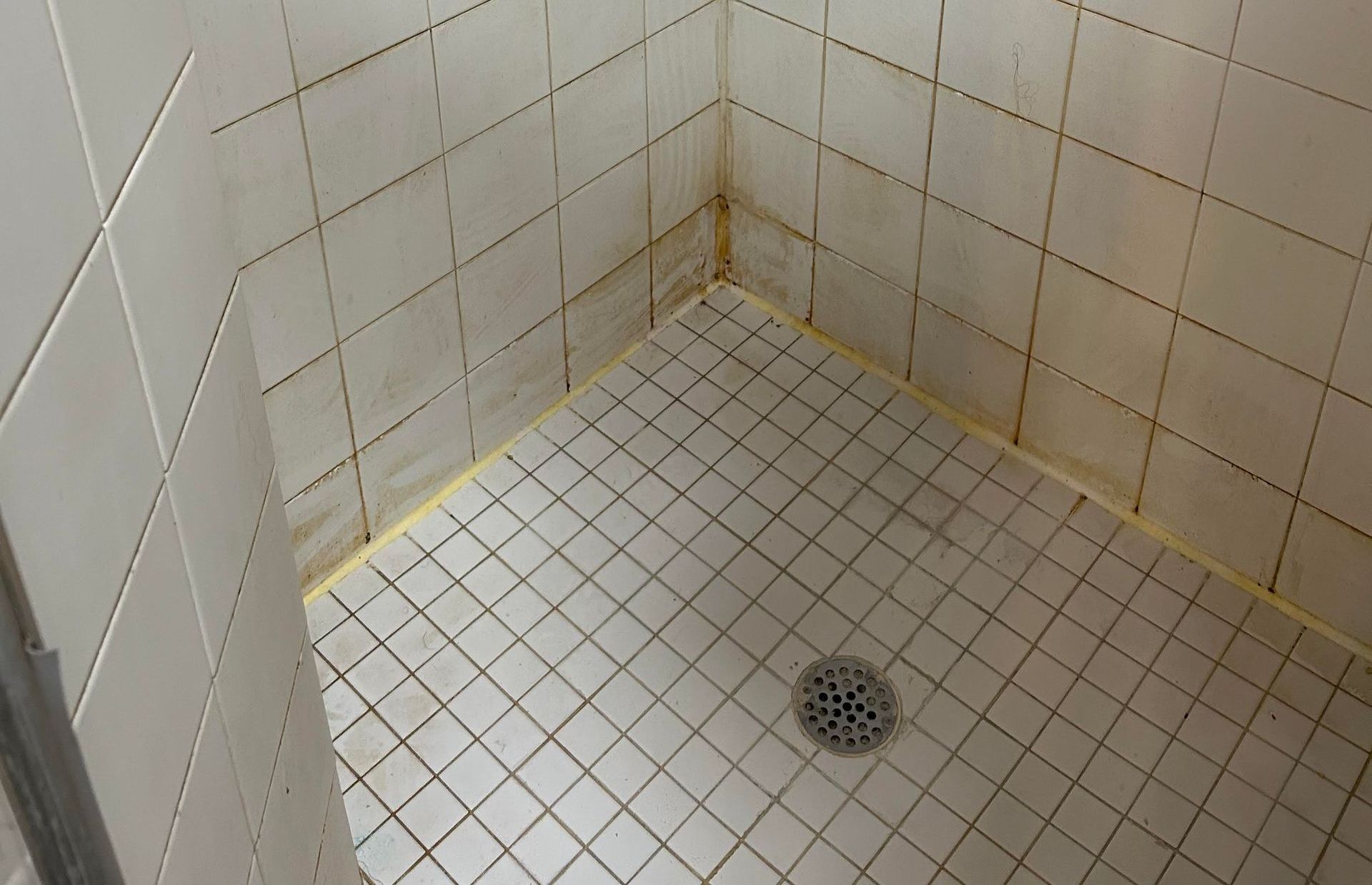 A shower stall with white tiles and a drain in the corner.
