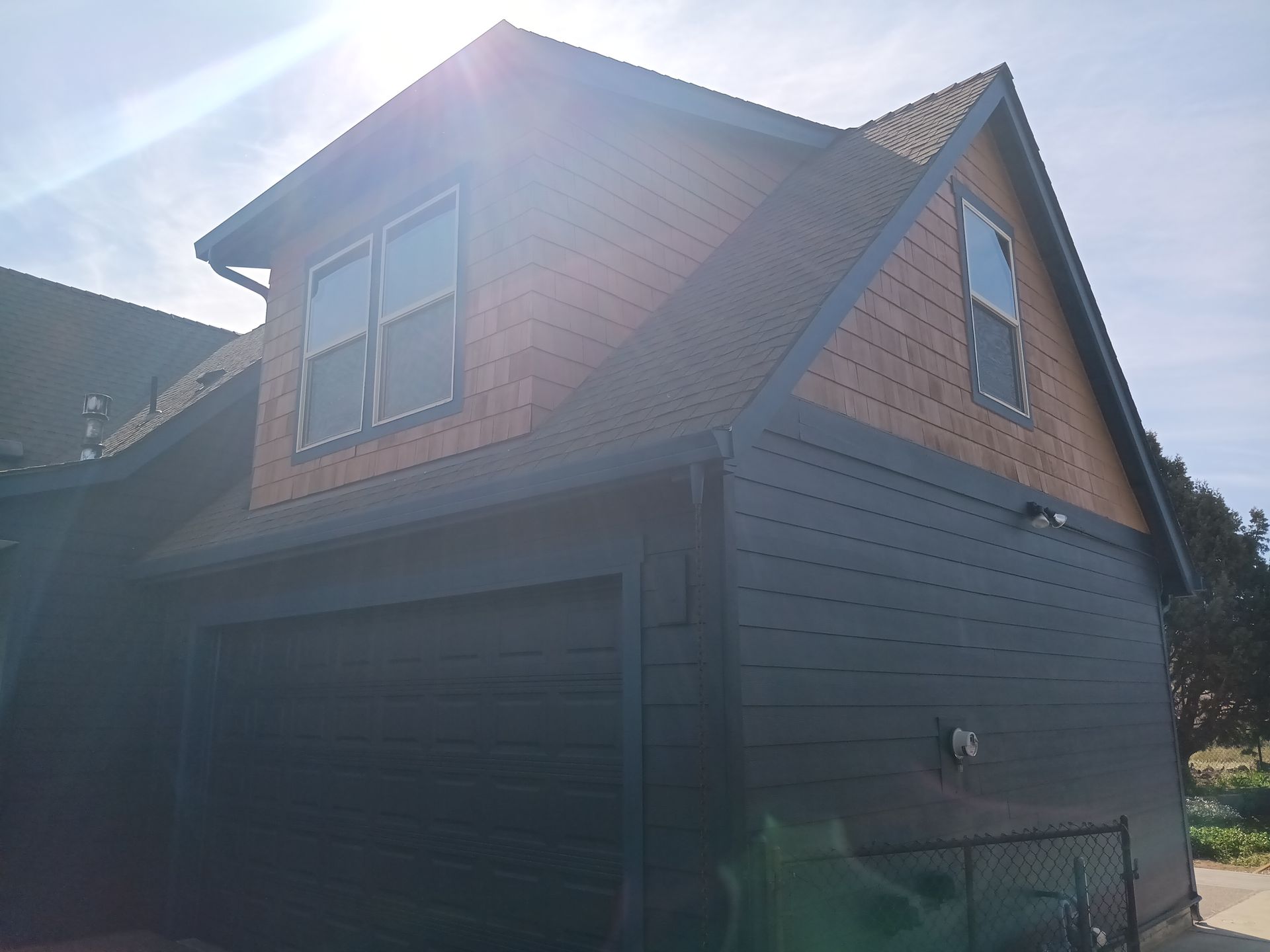Gray garage with a dormer window and brown shingled roof in bright sunlight