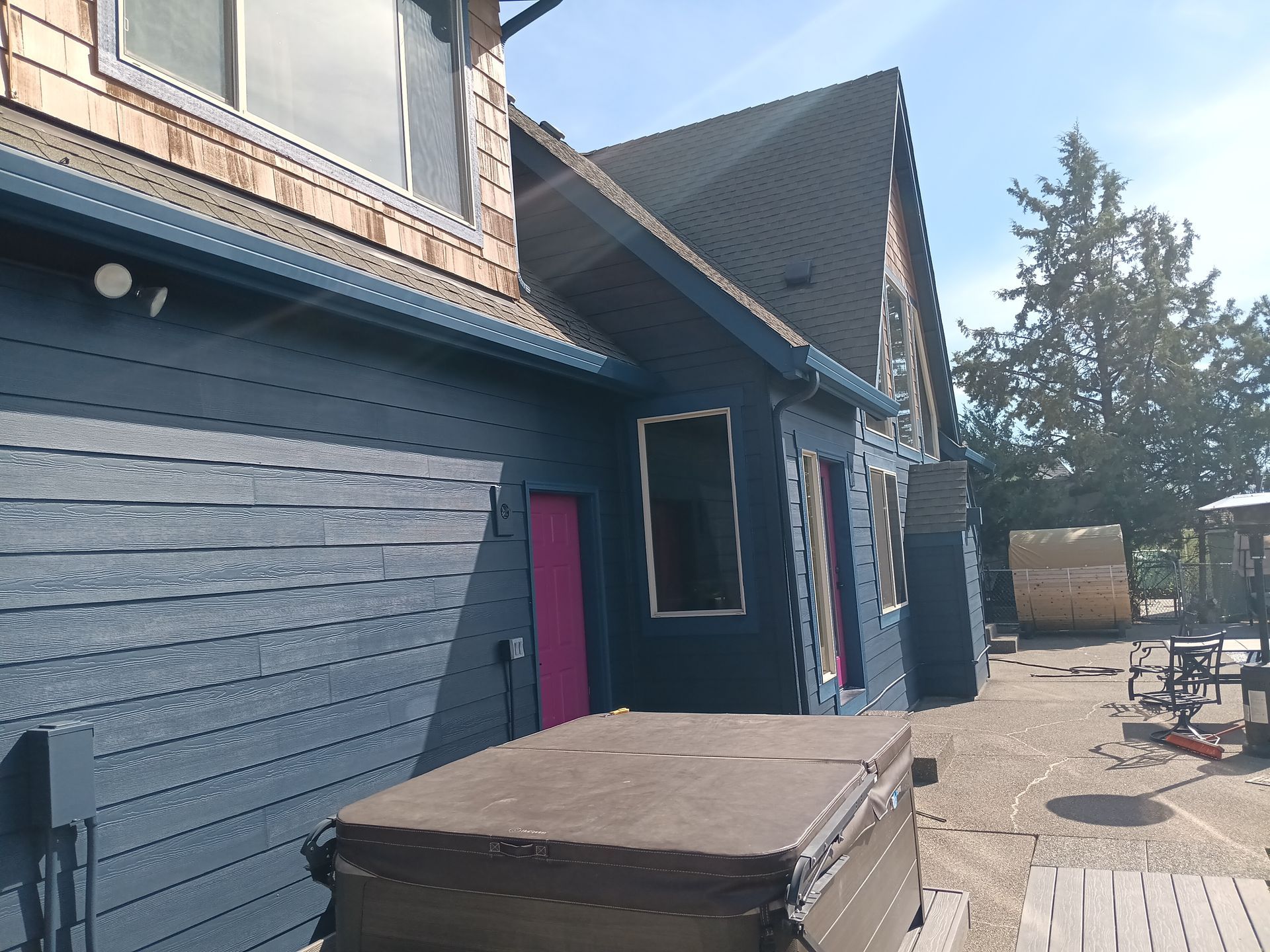 Blue house exterior with pink door, sloped roof, and patio furniture on a sunny day