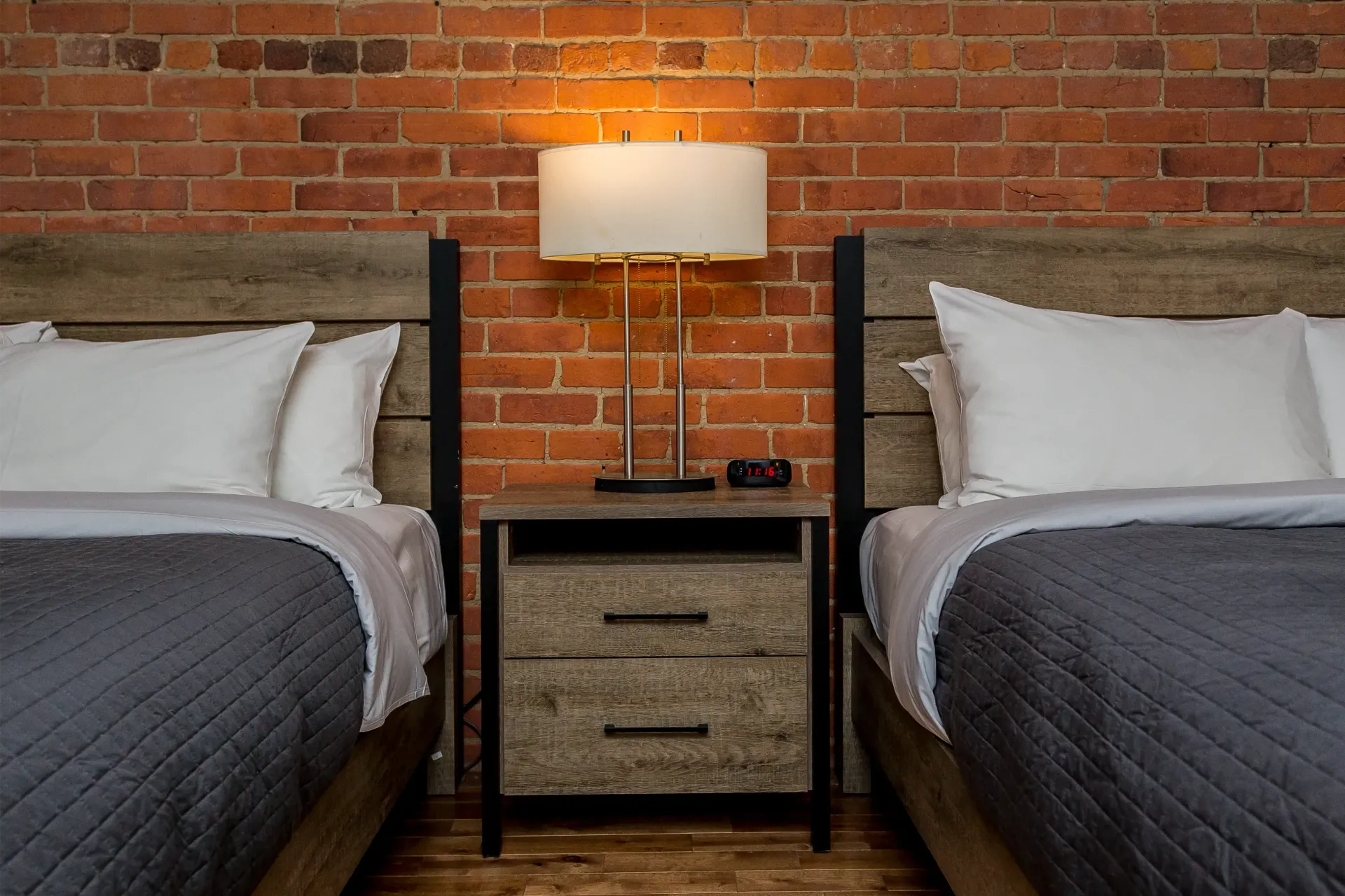 Deux lits et une table de chevet dans une chambre d'hôtel avec un mur de briques