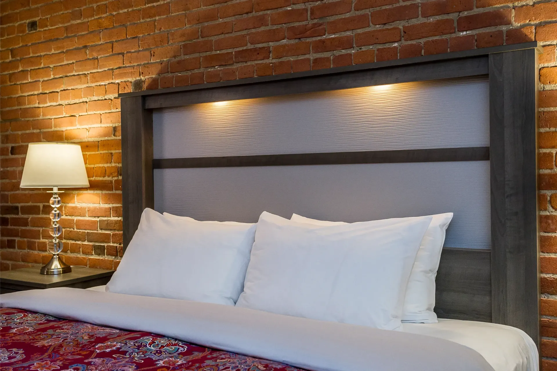 Un lit dans une chambre d'hôtel avec un mur de briques et une lampe