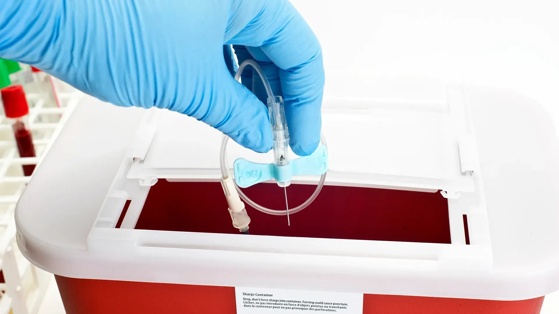 A person wearing blue gloves is putting a needle in a sharps bin.