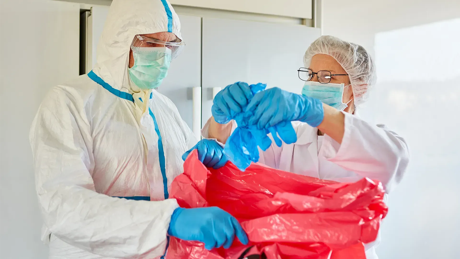 A man and a woman in protective suits are throwing away gloves.