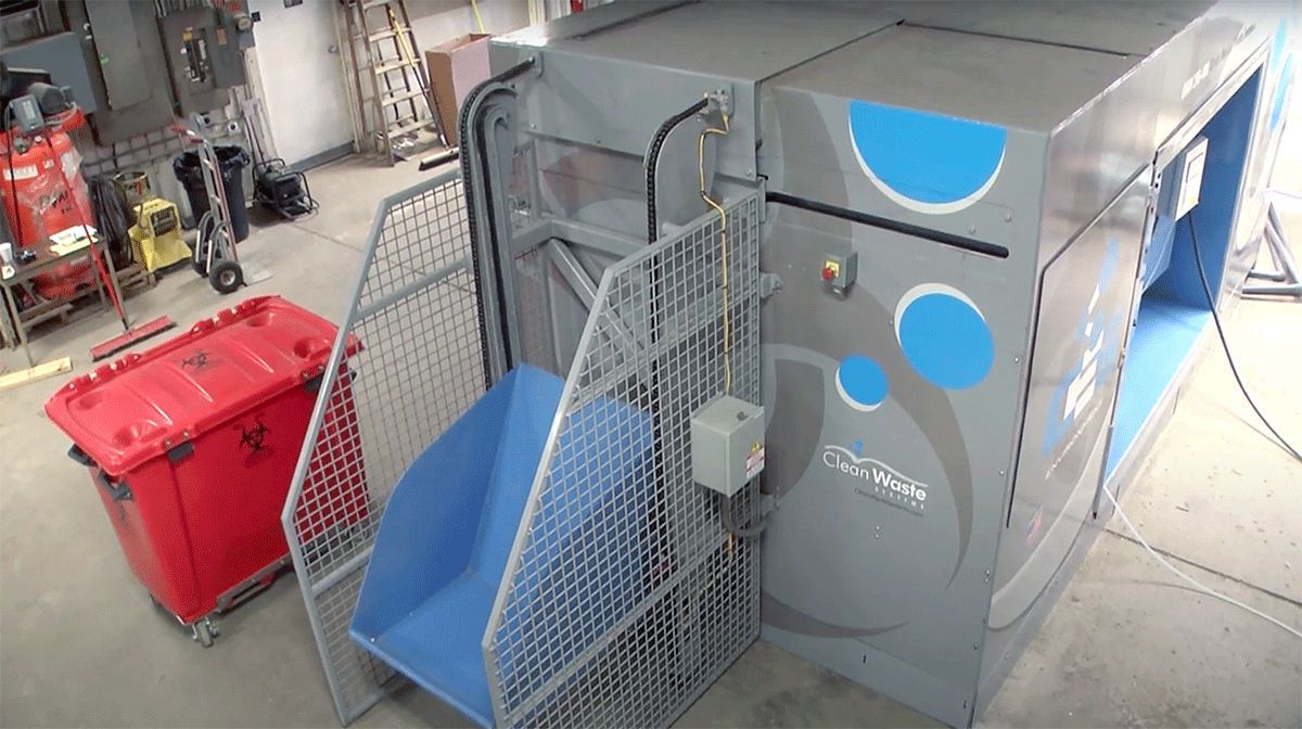 A machine with stairs leading up to it is sitting in a room next to a red trash can.