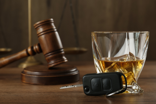 A glass of whiskey , a car key , and a judge 's gavel are on a wooden table.