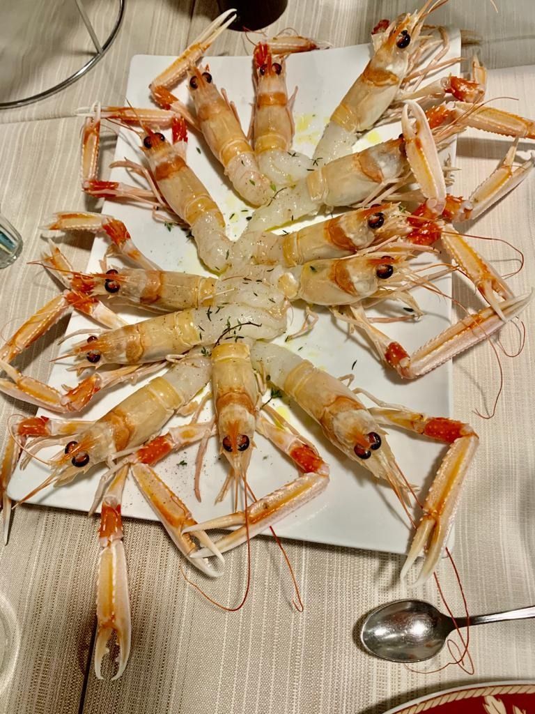 Scampi disposti su un piatto bianco, conditi con olio ed erbe aromatiche. Contesto della cena, primo piano.