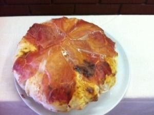 Pizza con prosciutto su un piatto bianco.