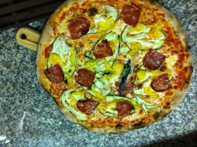 Pizza condita con pepperoni, peperoni gialli e zucchine su un tagliere di legno.