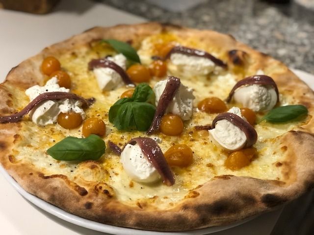 Pizza con acciughe, pomodori e basilico su un piatto bianco.