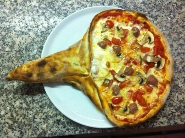 Pizza con un grande impasto ripiegato su un piatto bianco; i condimenti includono pomodori, funghi e salsiccia.