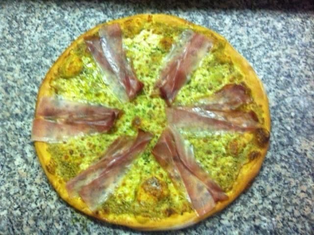 Pizza con salsa verde e fette di prosciutto su una superficie di marmo.