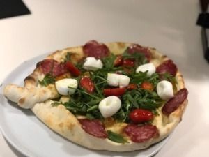 Pizza condita con salame, rucola, mozzarella e pomodori su un piatto bianco.