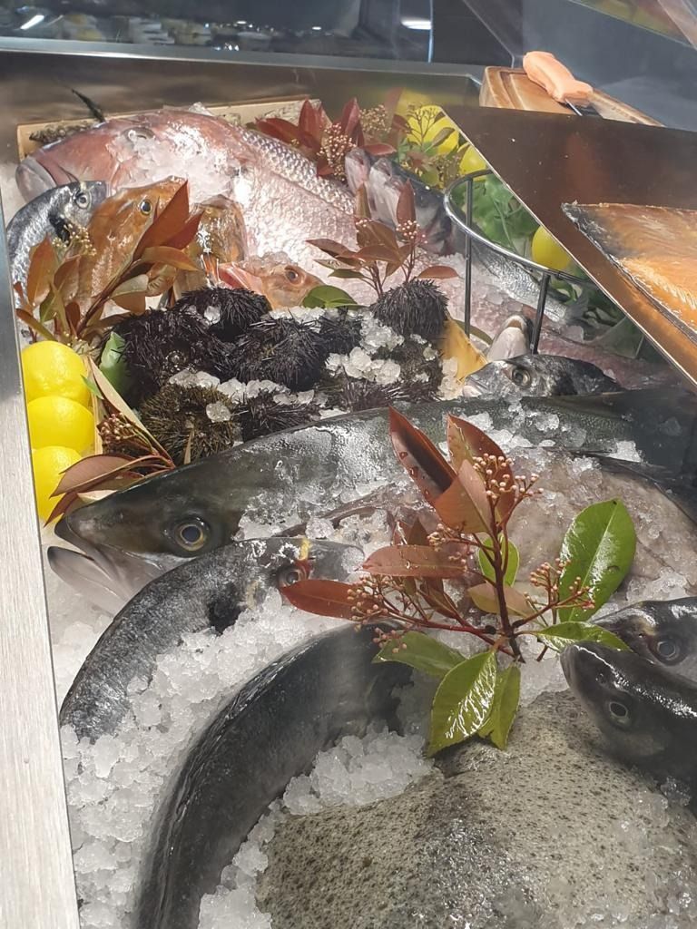 Esposizione di pesce fresco su ghiaccio con limoni e vegetazione decorativa.