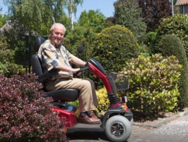 An elderly man is riding a mobility scooter on a sidewalk.