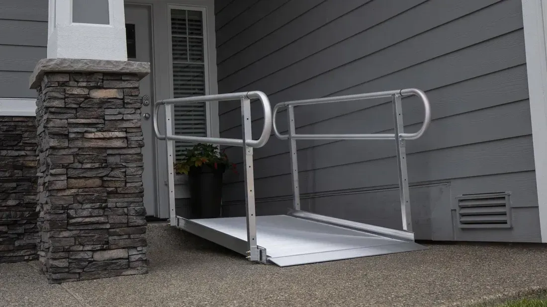 Aluminum ramp with handrails leading to a house entrance, aiding accessibility.