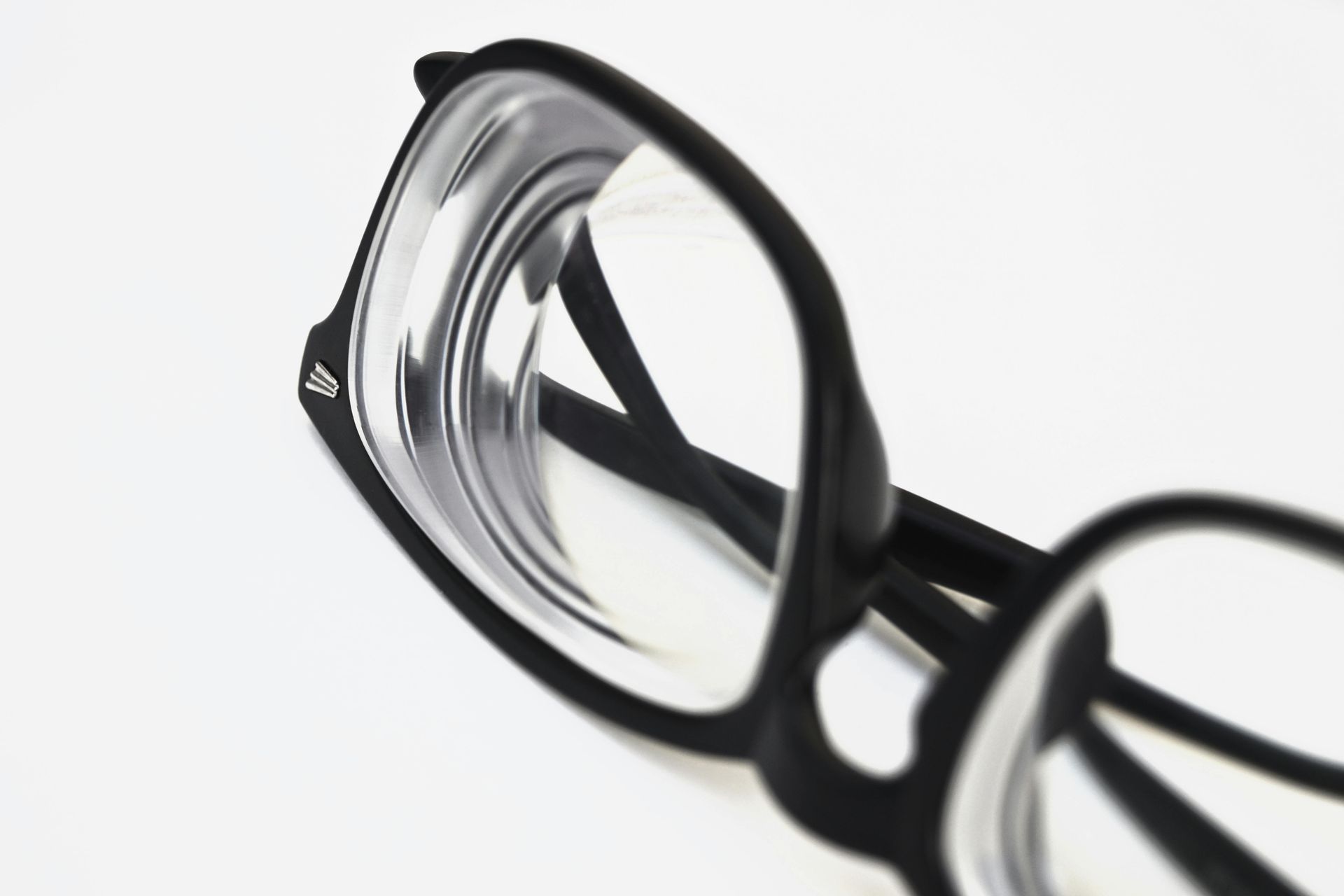 Black-framed eyeglasses resting on a white surface; lenses appear to magnify light.