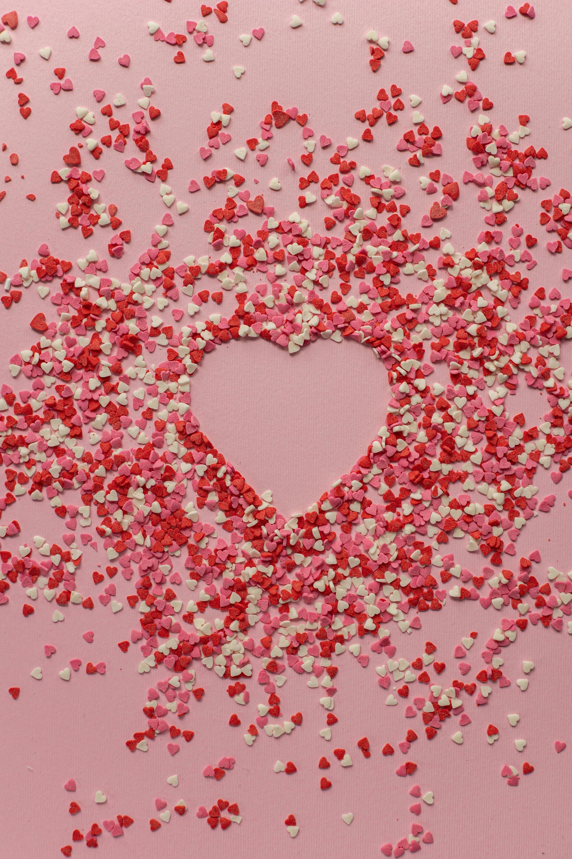 A heart made of pink and white sprinkles on a pink background.