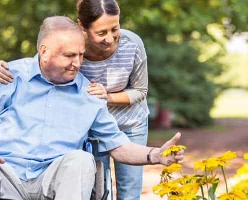 A woman is standing next to an elderly man in a wheelchair.